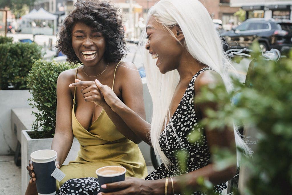 Two friends laughing together while enjoying hot drinks outside, embodying joy and companionship.