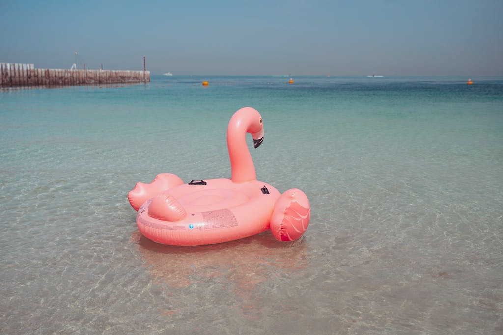 A vibrant pink flamingo inflatable floating on the clear waters of a Dubai beach.