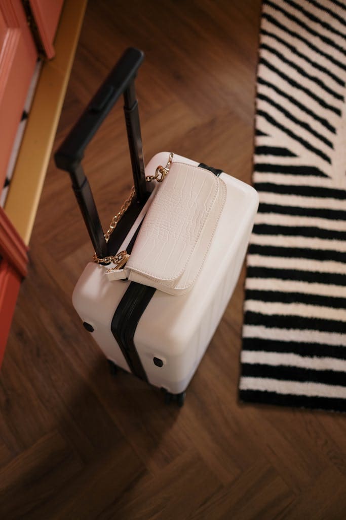 Top view of a white suitcase with a stylish handbag on a wooden floor with striped rug.