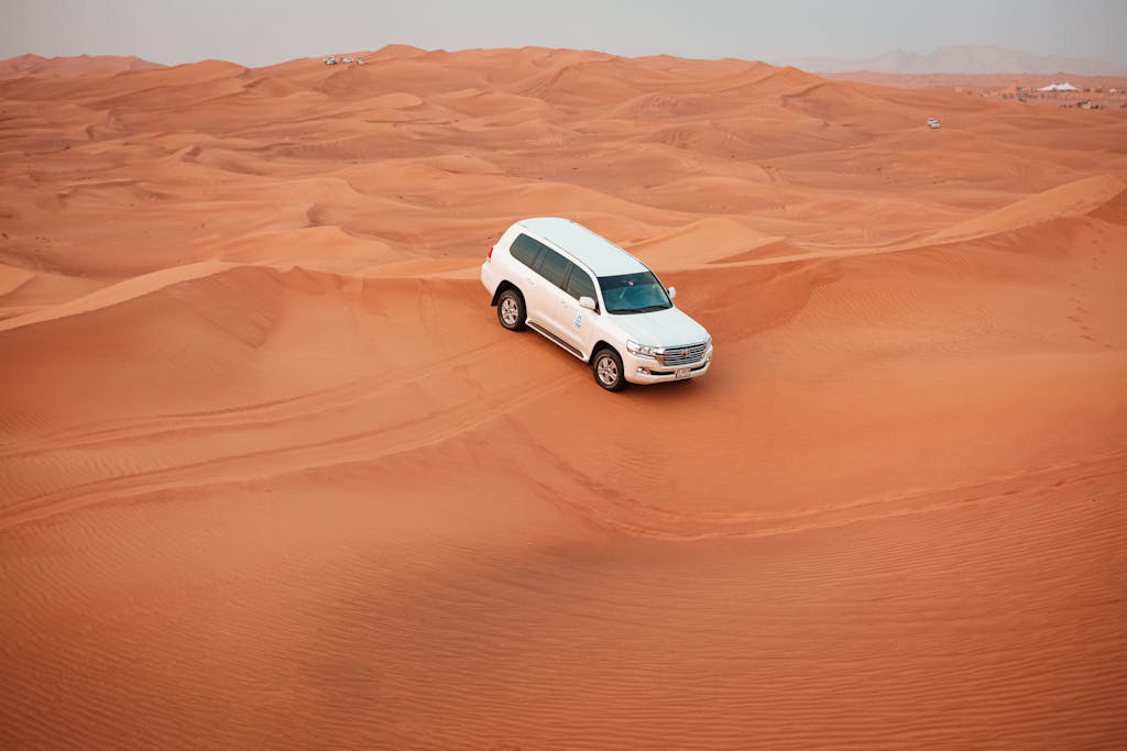 A white SUV drives through expansive sandy desert dunes, showcasing offroad adventure.